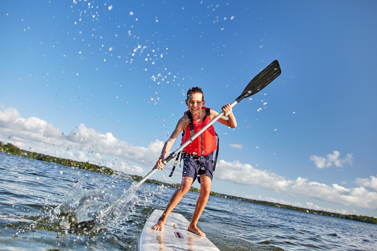 happy boy paddling on stand up paddleboard. cheerful child having fun on water. Summer vacation leisure activity